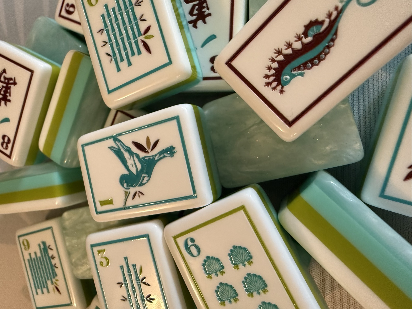 Macro closeup of the one-bam tile showing a teal hummingbird in flight, beside a seahorse tile, in the coastal mahjong set