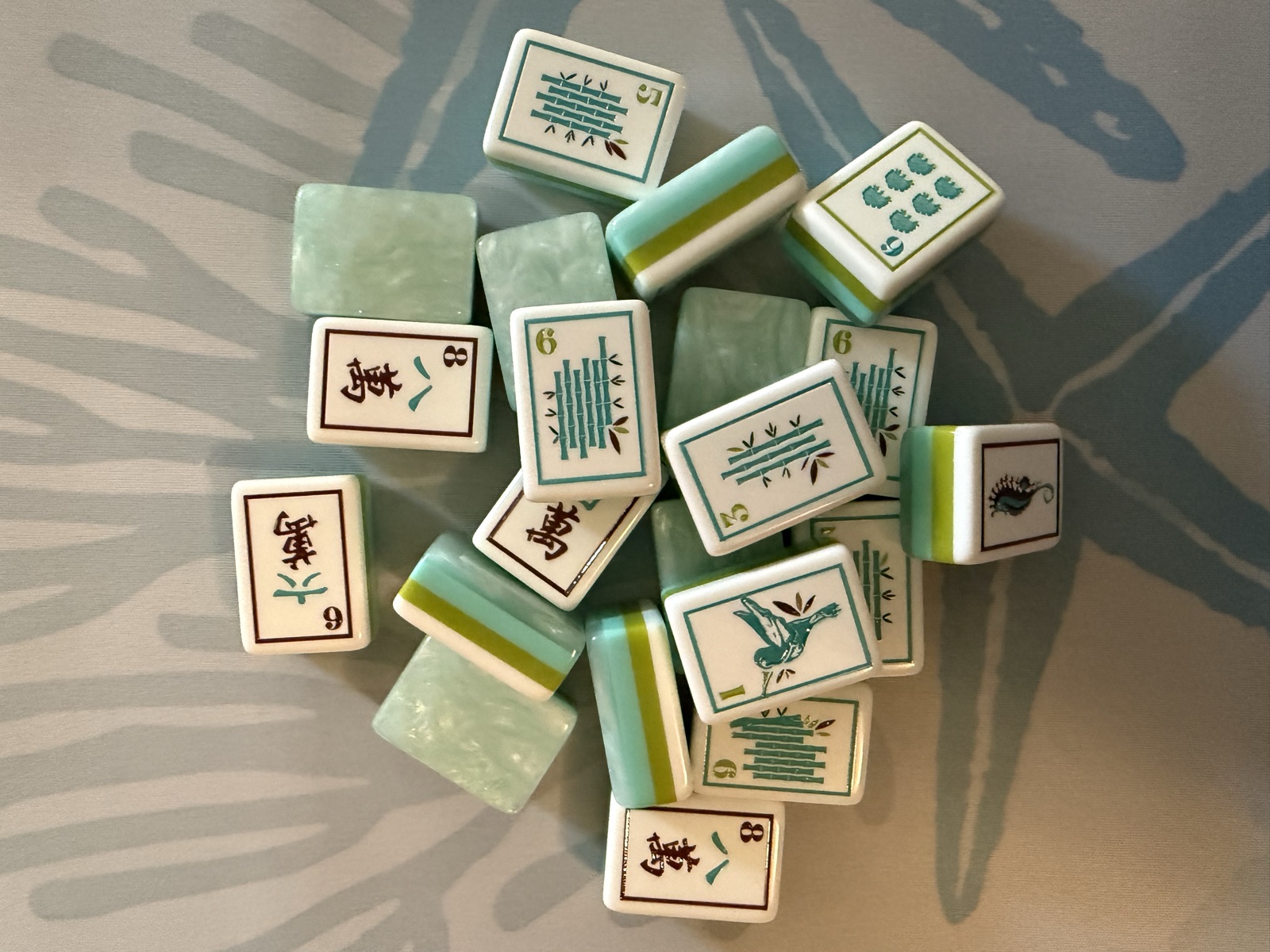 Overhead view of the beach mahjong tiles spread out, showing bamboo, character, seahorse, and seashell tile artwork in teal and green