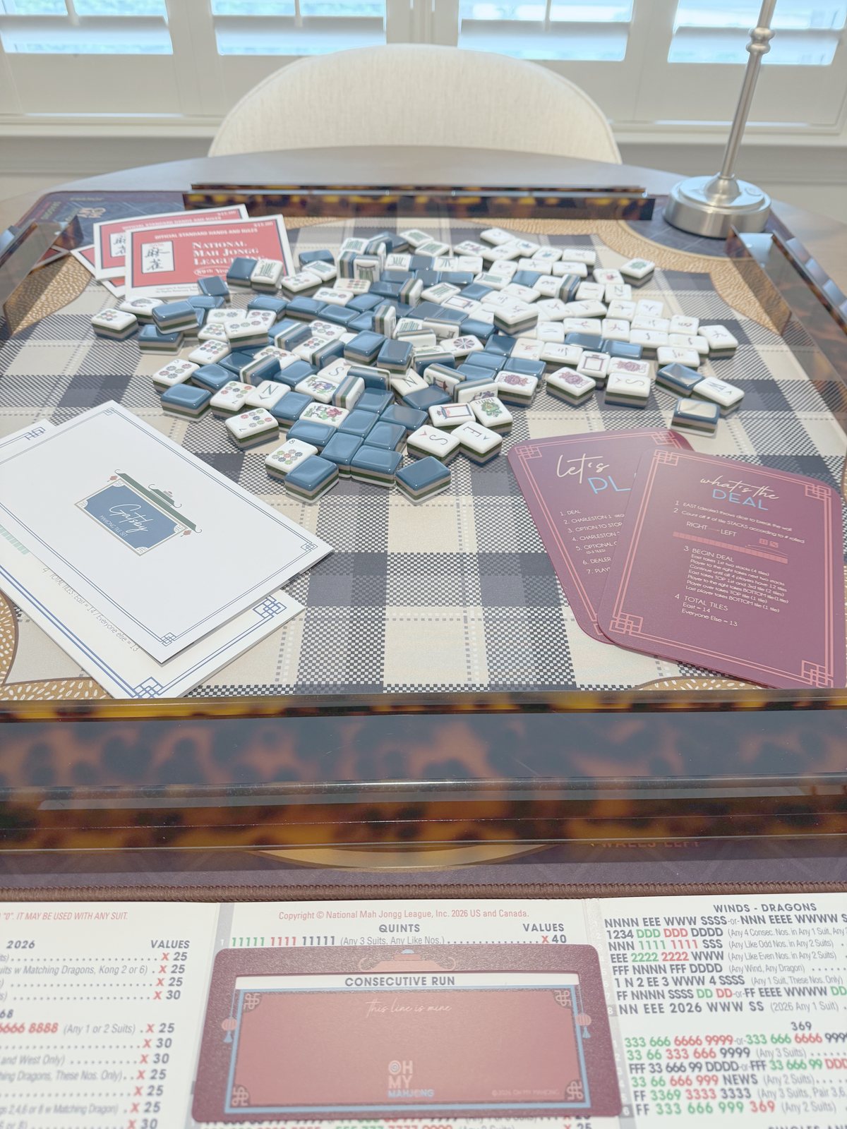 Overhead view of deep navy Oh My Mahjong Gatsby tiles spread across a navy buffalo-check mat with tortoiseshell racks
