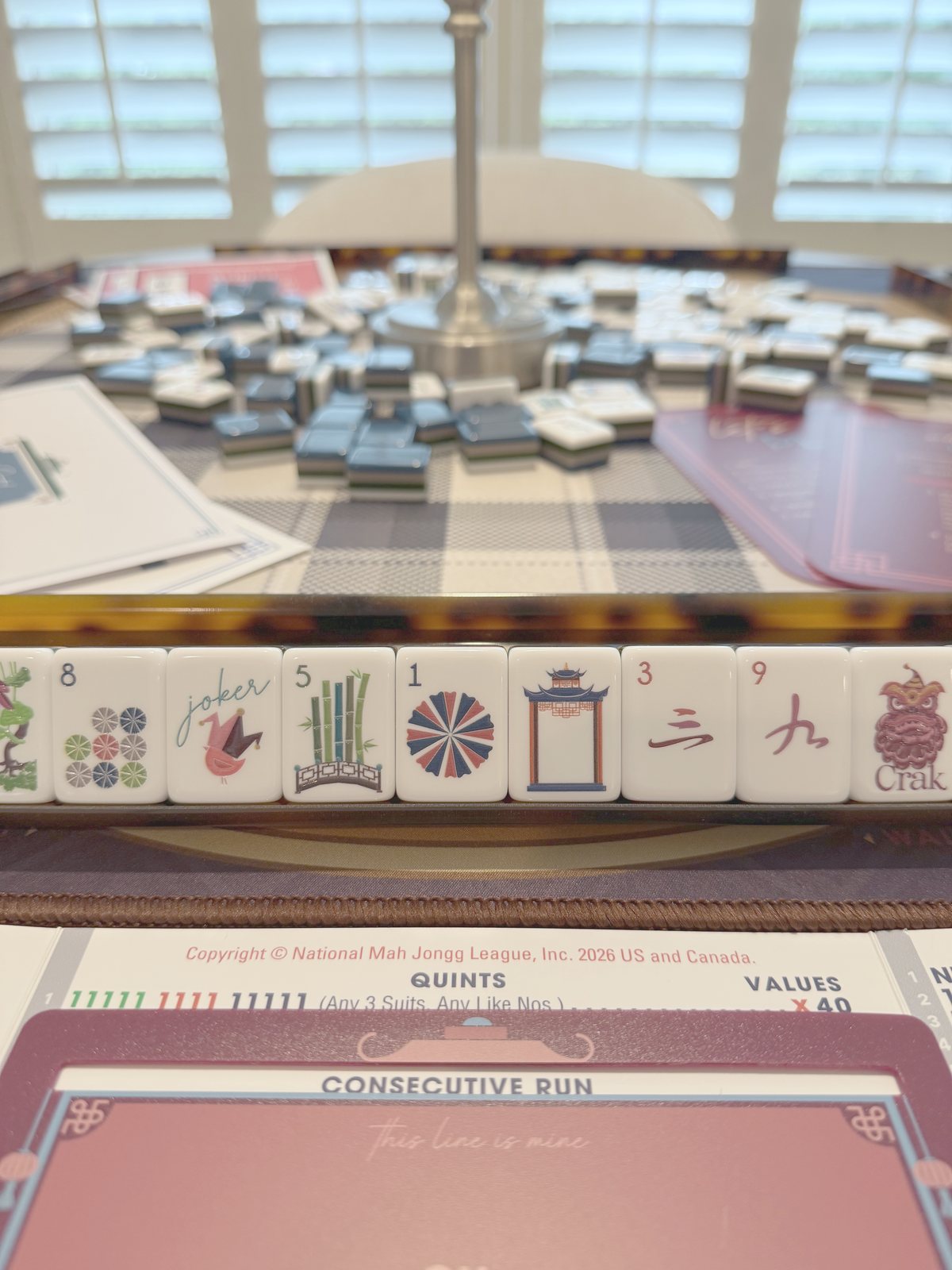 Closeup of navy Gatsby tiles in a tortoiseshell rack beside the NMJL card on the navy buffalo-check mat