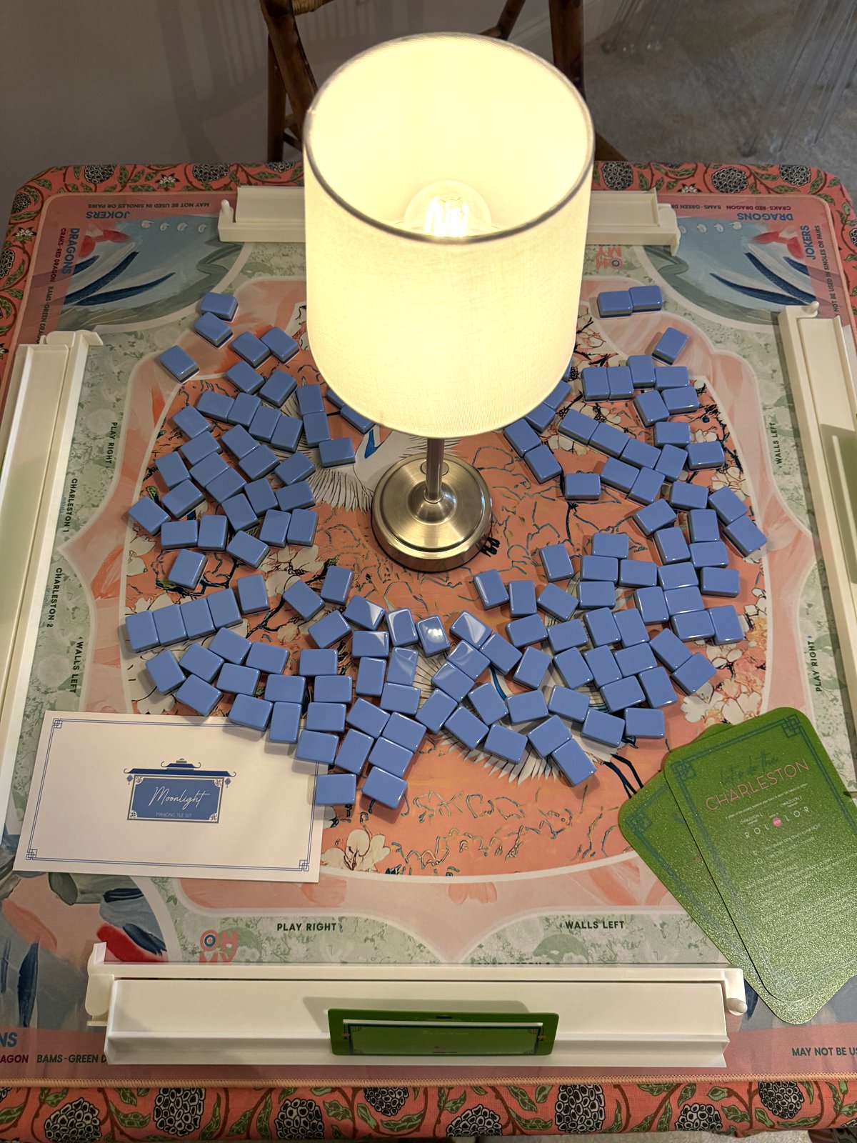 Overhead view of cornflower-blue Moonlight tiles spread across the coral chinoiserie Heron mat, with cranes in the corners and a 'Moonlight' place card