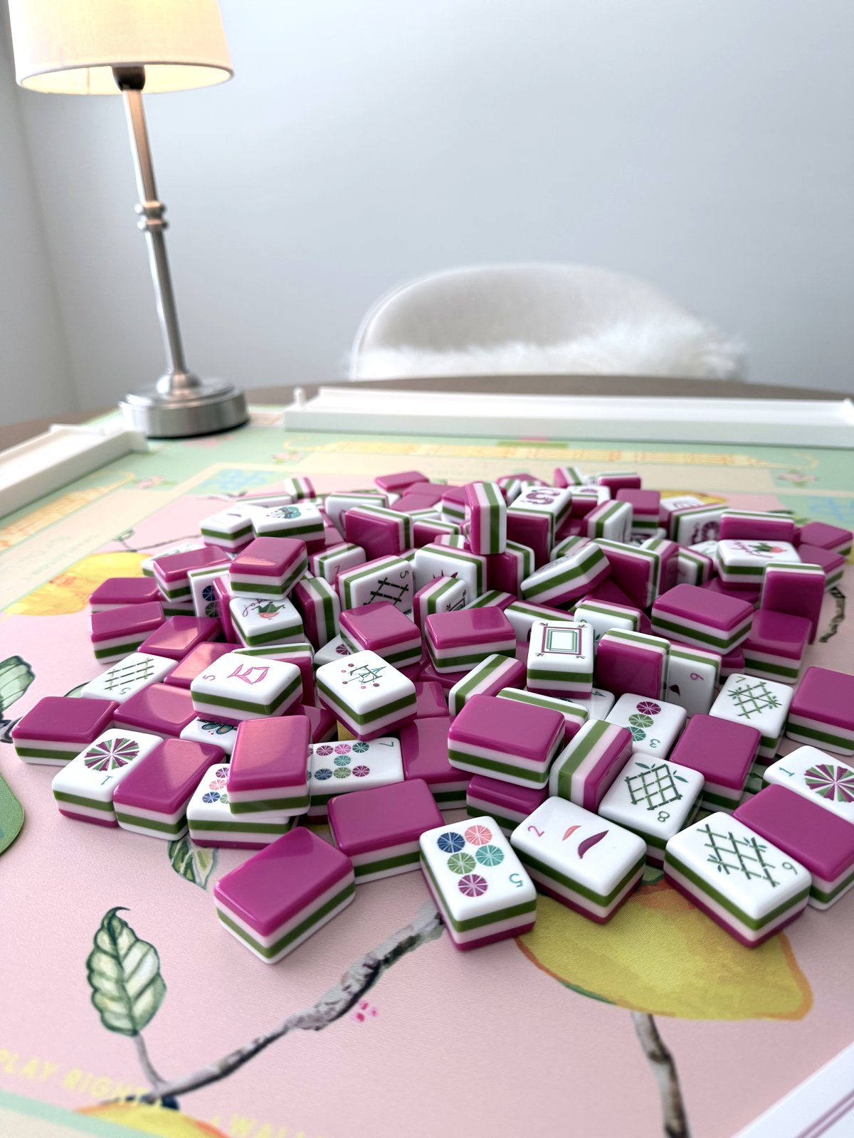 Closeup of Oh My Mahjong Dandy tiles with magenta-and-green striped edges over white faces and colorful dot, bamboo, and flower symbols on the Citrus Songbird mat